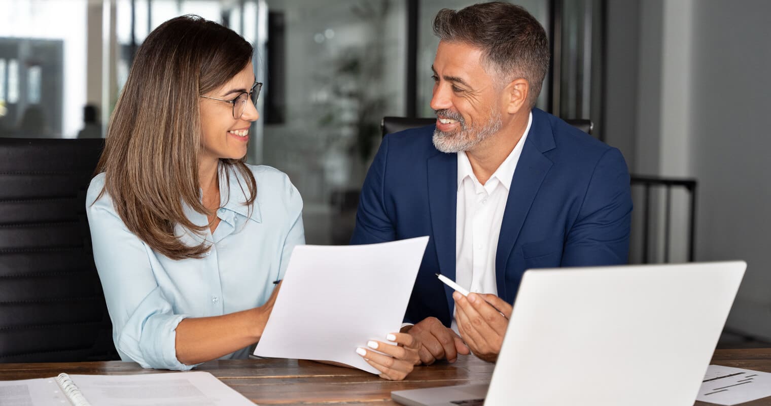 Two friendly co-workers discuss data transformation at a modern office desk.