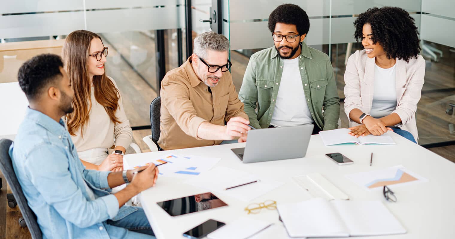 A team collaborates around a laptop, engaged in discussion. The scene reflects a modern workspace, emphasizing no-code development.