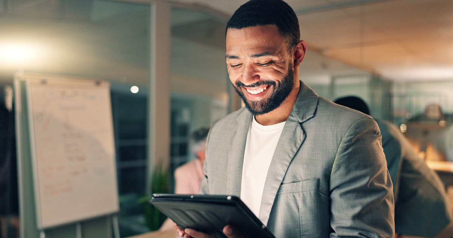 A smiling man in a suit uses a tablet in an office, illustrating the concept of orchestration in data management.