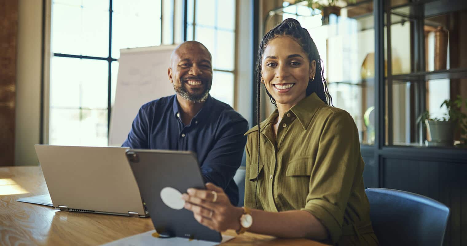 A man and woman smiling and working together on laptops and tablets, discussing connected apps.