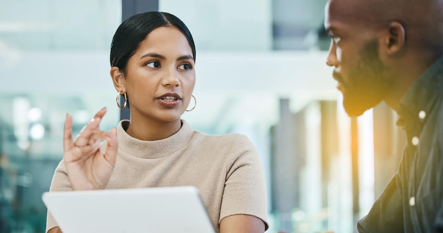 Woman explaining Enterprise Data Architecture concepts to a colleague in a modern office setting.